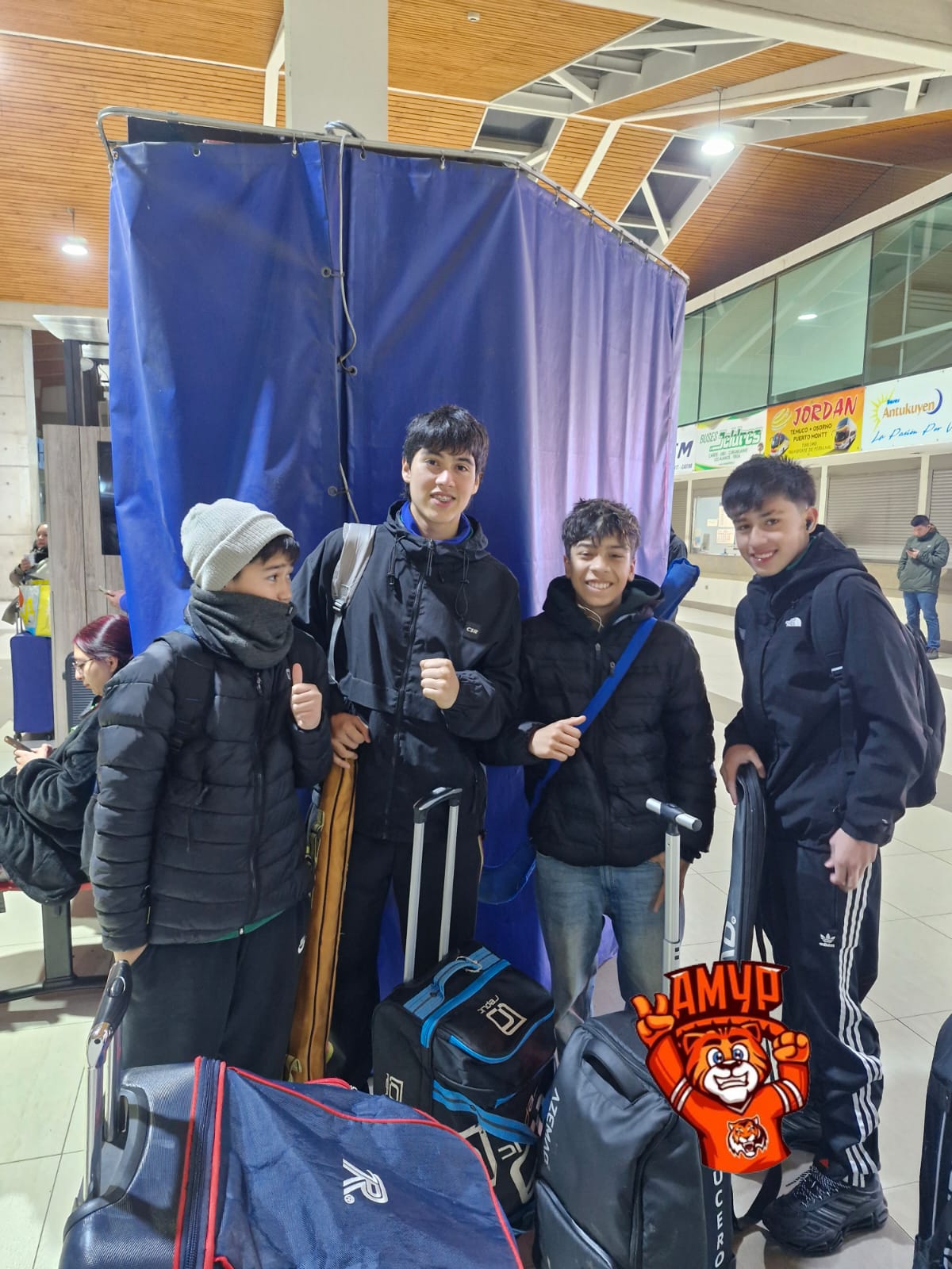 Cuatro niños jugadores de hockey patín de Talcahuano en un terminal de buses de noche, con sus bolsos y equipamiento, listos para viajar a Santiago